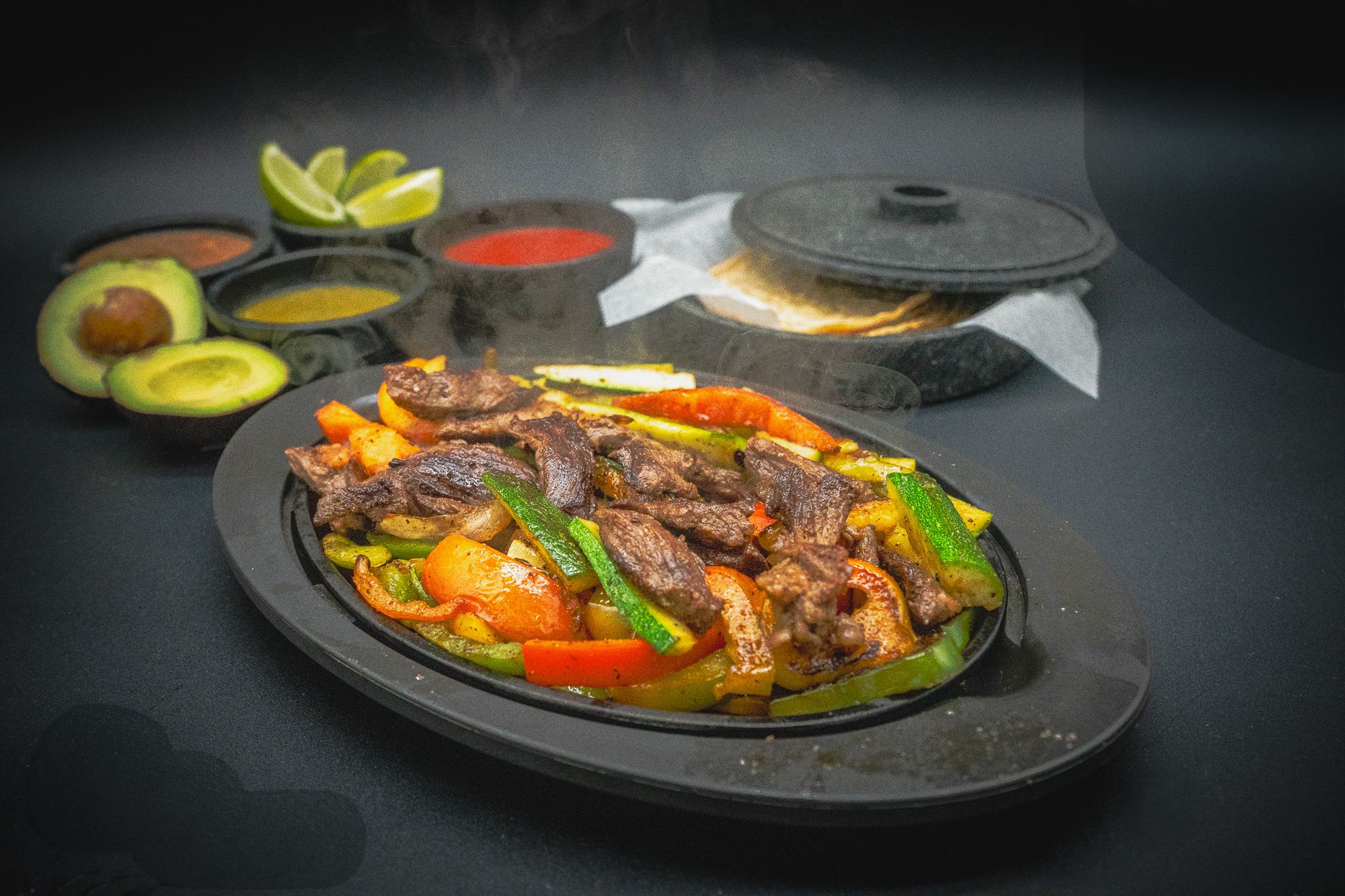 Fajitas on a sizzling skillet with tortillas, guacamole and salsas